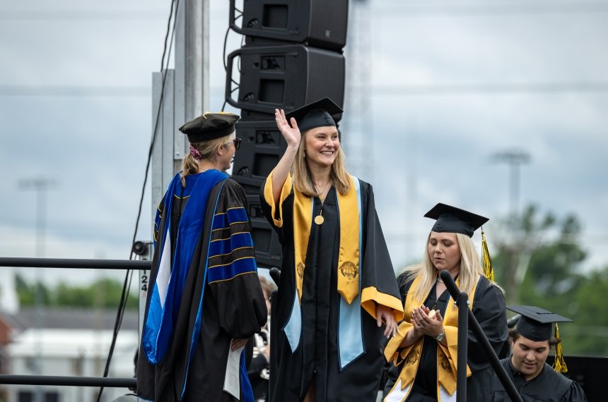 Lucy Triebsch walking across the graduation stage, waving to the crowd