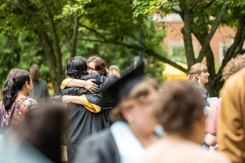 Two graduates hug in the middle of a crowded lawn