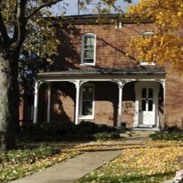 Multi level brick home with wrap around porch and thin columns on front porch. Sidewalk leading up to porch. 