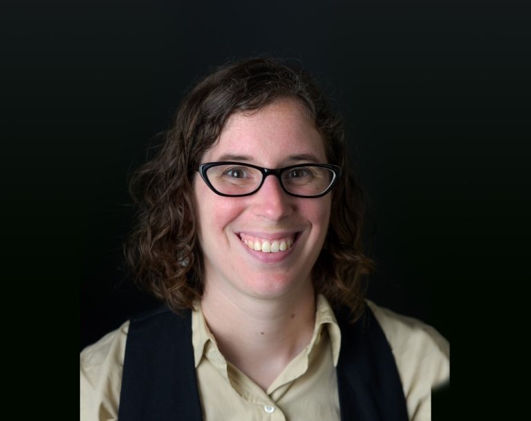 Lady with short brunette hair with beige top and black scarf on top in front of black background