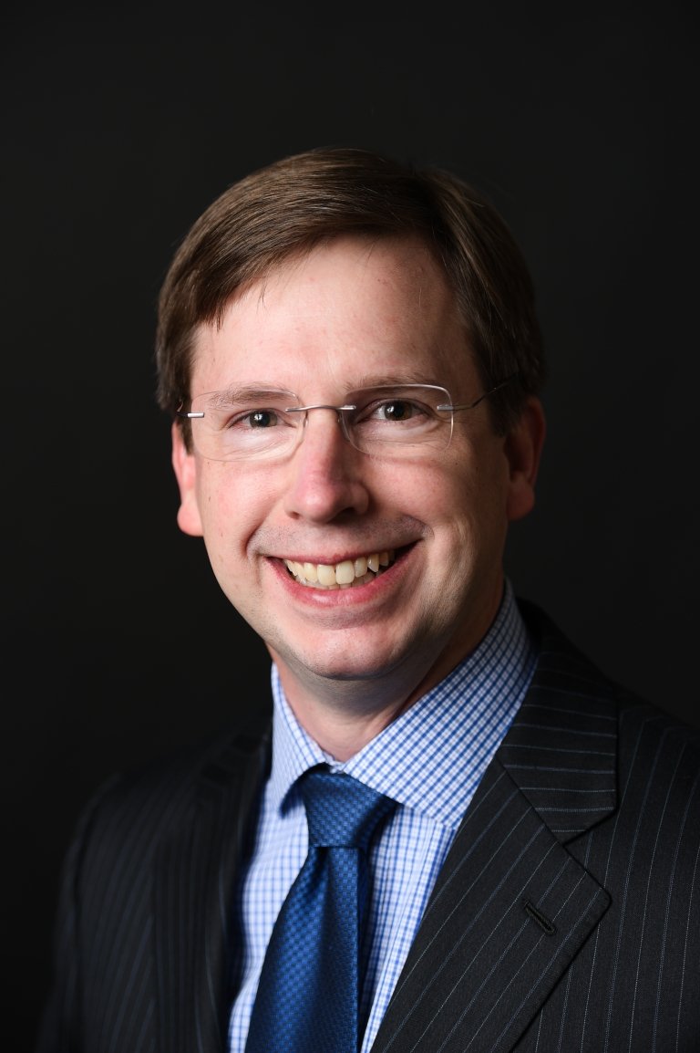 Thomas Allen - man with dark hair wearing glasses and black suit, blue gingham shirt, and navy tie