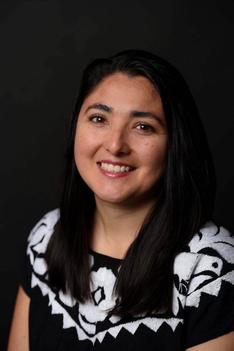 Lady with dark hair wearing black and white top in front of black background