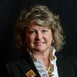 Person wearing dark jacket with centre logo lapel pin 