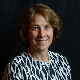 Person wearing navy and white top in front of dark background smiling