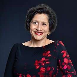 Person wearing black and red shirt standing in front of dark background smiling