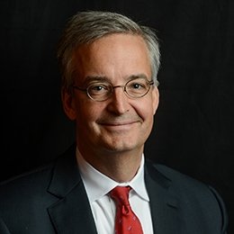 Person wearing dark suit jacket and red tie smiling 