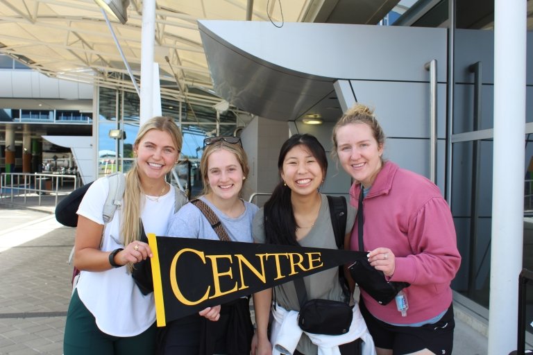 Four students hold a Centre College pennant while posing for a photo.