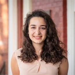 Lady with dark curly hair wearing peach top standing on front porch of ODI building 