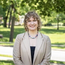 lady with short curly hair wearing khaki blazer and black top with necklace