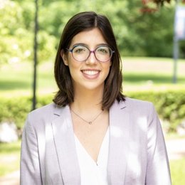 lady with dark hair wearing light pink blazer and white top with glasses and necklace