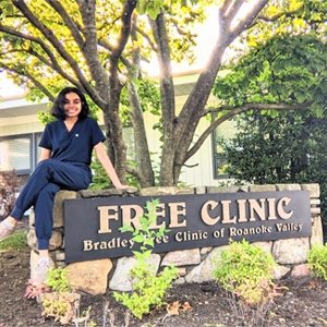 Srija Badireddi, a student sitting on the sign for Free Clinic of Roanoke Valley