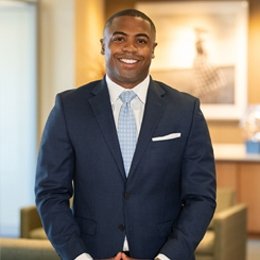 Man wearing navy suit and light blue tie standing inside library