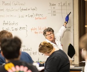 Professor teaching microbiology class wear white coat and blue gloves point on the white board