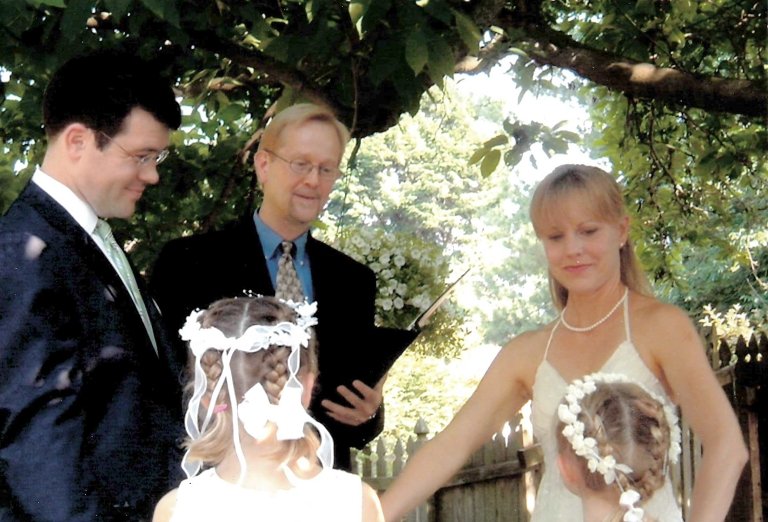 A bride, groom and officiant look at two small girls taking part int the wedding ceremony.