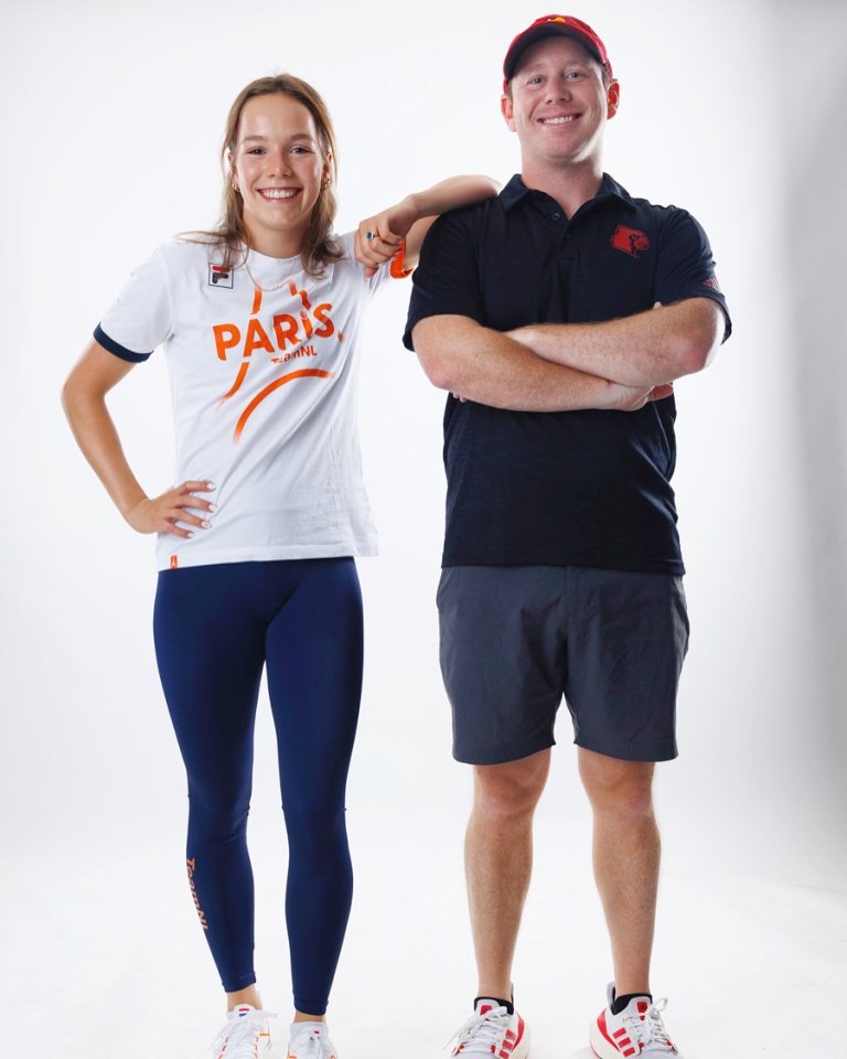A woman and man post together for a photo in front of a white backdrop. 