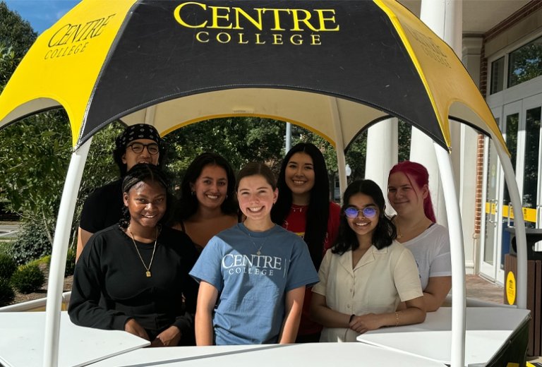 Centre students group photo standing under hut smiling at camera