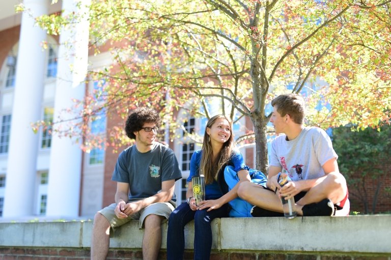 Three students sit on a wall, talking
