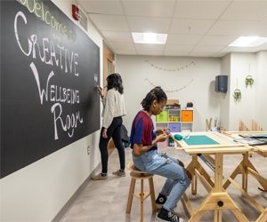 Student drawing on chalkboard and another student using clay at a desk