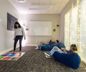 Students sitting on bean bag chairs listening to music and another student interacting with color board on the floor