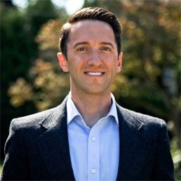 Person wearing dark jacket and blue shirt smiling 