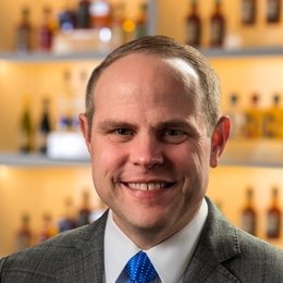 Person standing in front of shelves of bourbon and smiling 