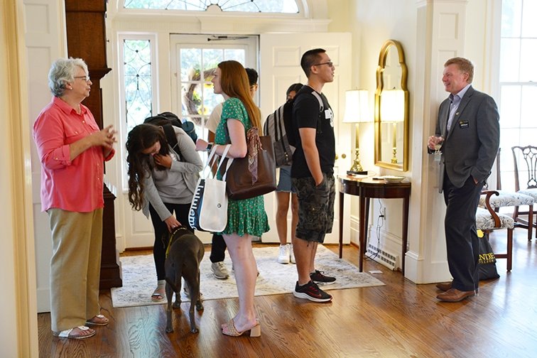 A woman and a man stand on each side of a home's entryway, greeting guests as they arrive.