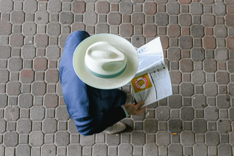 A man looks down at the betting program. His head is obscured by a wide-brimmed fedora.