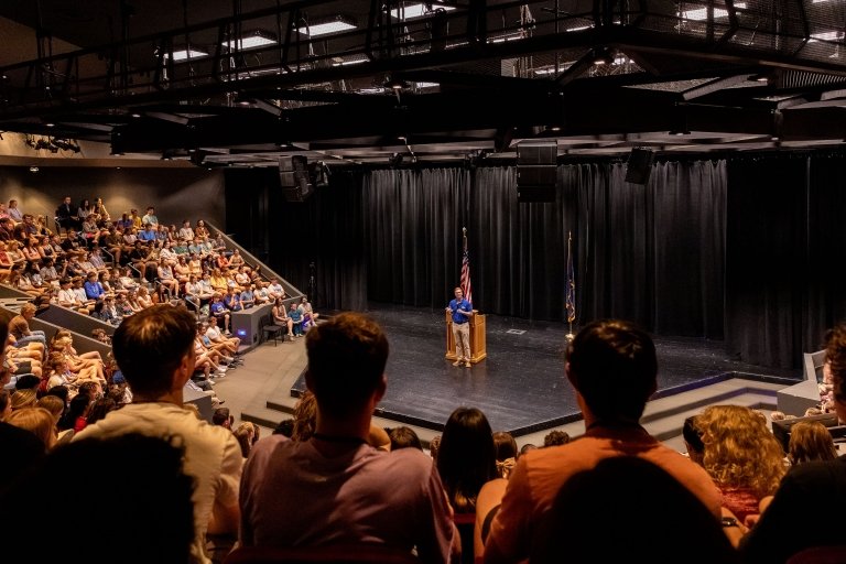 High school students listen to Andy Beshear speak on stage.