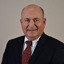 Person wearing suit and tie in front of beige background