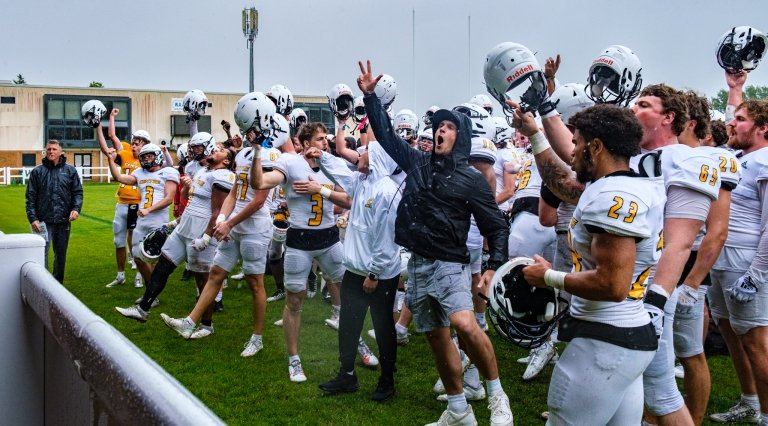 Football players and coaches on a green field waving.