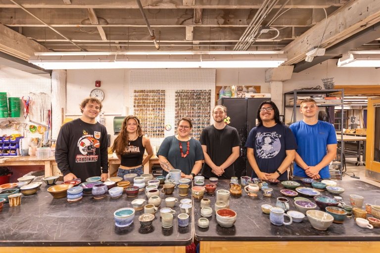 Stephanie Galli with five students with their ceramic pieces laid out before them on a table.