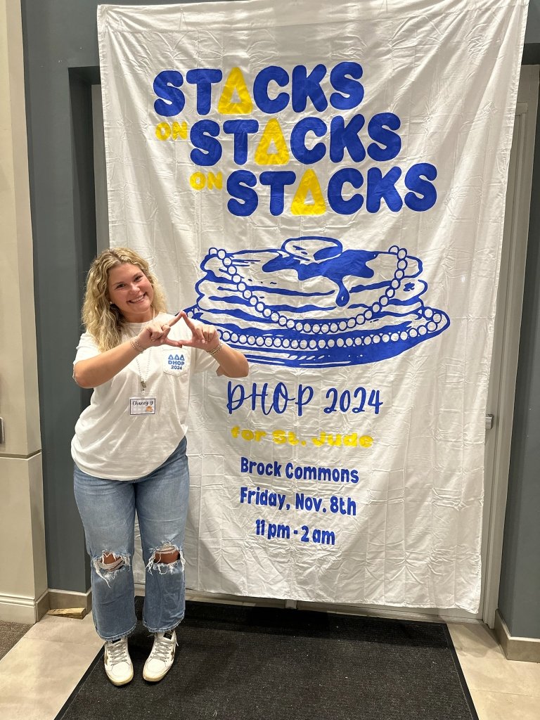 A Tri-Delta leader standing in front of a sign for their DHOP fundraiser.