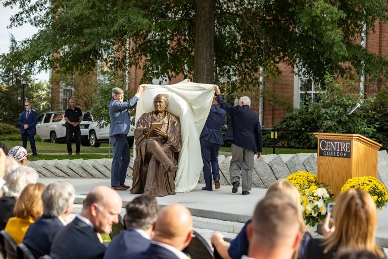 Harlan statue is being revealed by three individuals at the dedication ceremony.