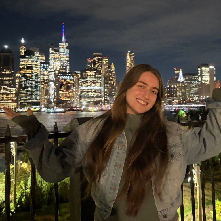 Anna is smiling and posing in front of the NYC night skyline.