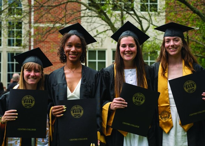 Four students holding graduation certificates and smiling at photographer