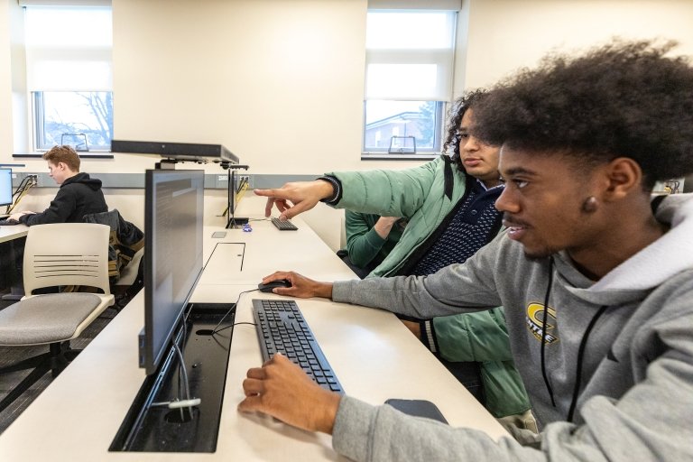 One Centre student points to a computer screen as a classmate in Professor Thomas Allen's AI class works on a coding project in the computer lab. 