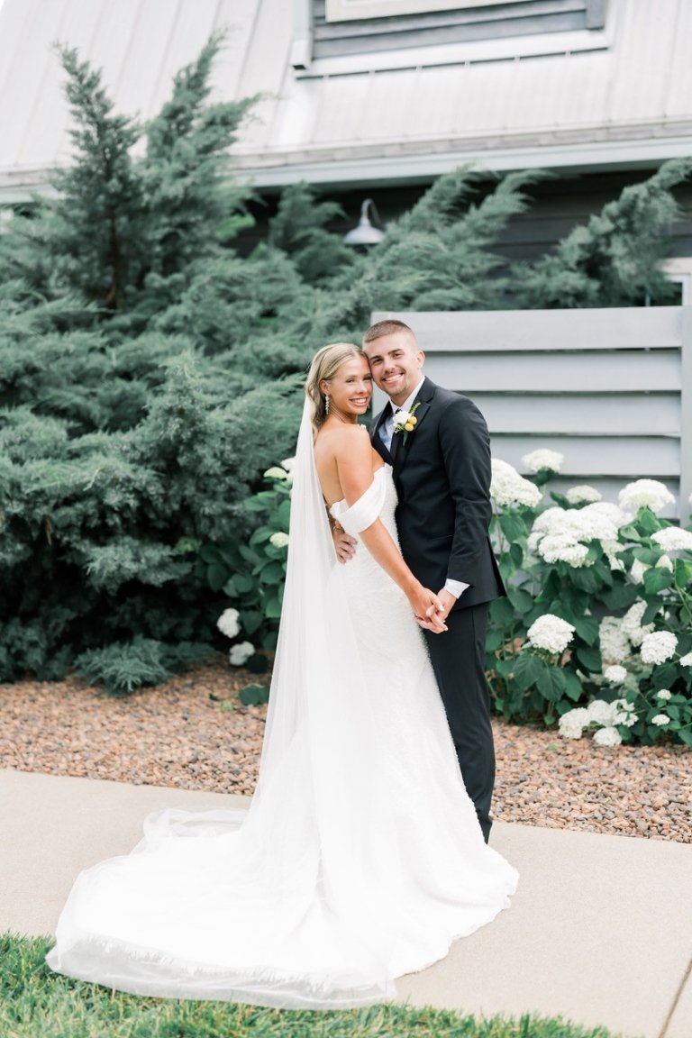 Binion's wedding photo. She is wearing a white gown with a train and he is in a tuxedo.