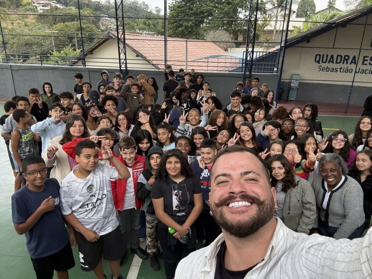 Matheus Marlisson smiles as he takes a selfie in front of a large group of young students at a Brazilian school. 