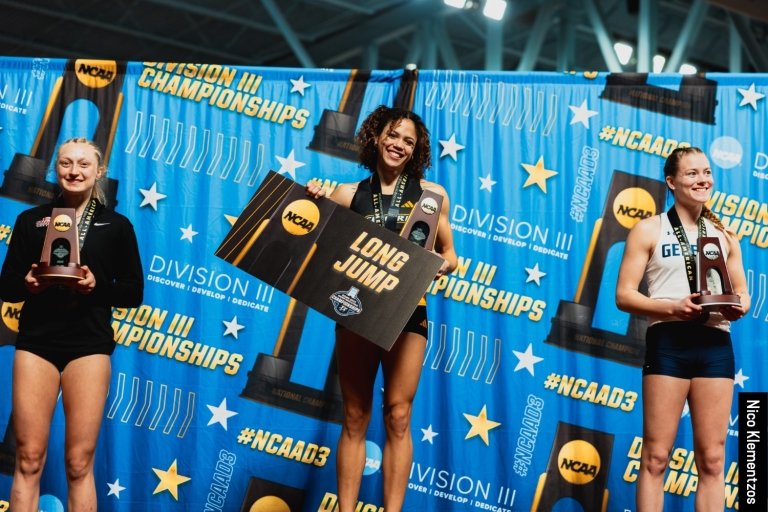 Chloe Heins standing on the podium holding her trophy and long jump sign.