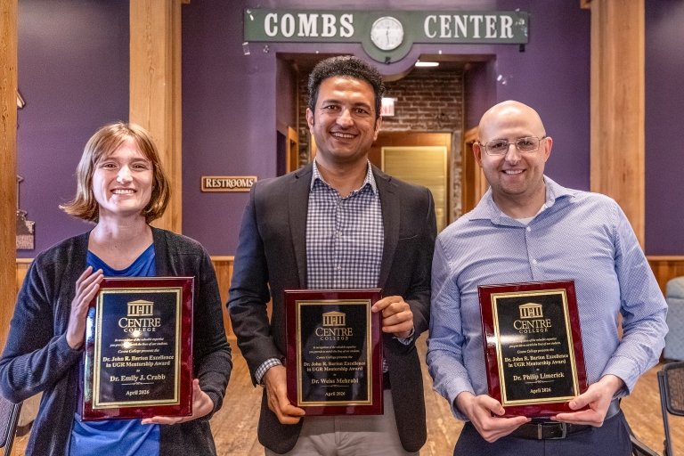 A woman and two men pose together, each holding a plaque of recognition naming them recipients of the Dr. John Barton Excellence in Undergraduate Research Mentorship Award.