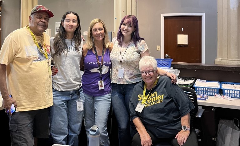 A man and four women stand arm-in-arm posing for a photo.