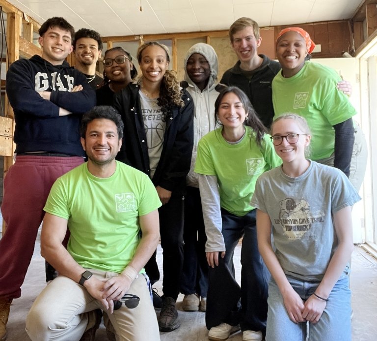 A group of eight students along with once Centre staff member and a member of the Centre faculty pose for a photo inside a house that is being stripped prior to renovation. 