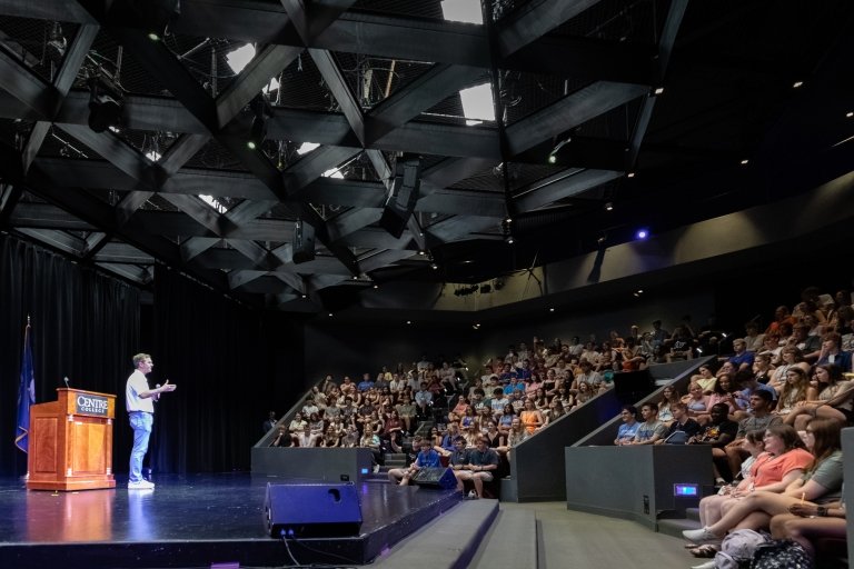 Kentucky Gov. Andy Beshear speaks into a microphone as an auditorium full of high school students look on.