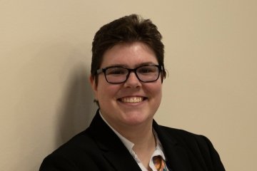 Lady dark short hair wearing sports coat and button up dress shirt and glasses