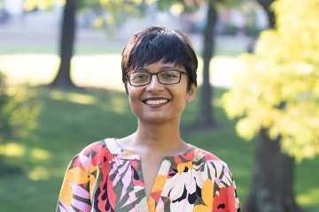 Lady with short dark hair wearing glasses with multi color patterned top