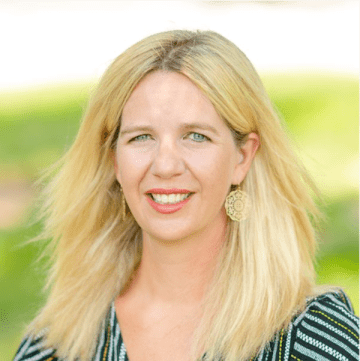 Lady with blonde shoulder length hair wearing gold earings and multi color navy top