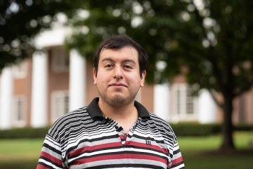 Man with short dark hair wearing multi color striped polo shirt in front of Old Centre