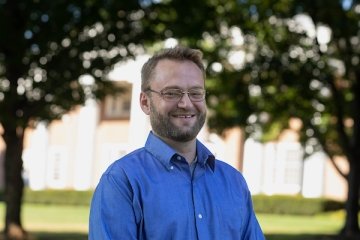 man with sandy blonde hair with beard wearing glasses and blue button up shirt