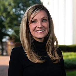 Lady with dark blonde hair wearing black sweater standing outside on campus