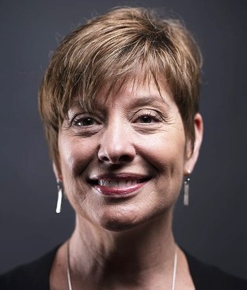 Lady with short brown hair, long earrings and necklace, wearing black top